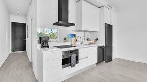 Une cuisine moderne avec des meubles blancs, une hotte noire, un four encastré et un réfrigérateur.