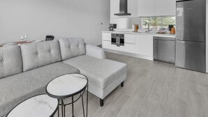 Une cuisine moderne avec un canapé gris, une table à manger et un grand réfrigérateur.