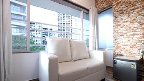 A modern living room with a white sofa, a compact refrigerator, and a brick wall.