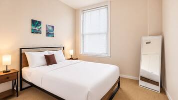 A hotel room with a bed, bedside tables, a window with blinds, and artwork on the wall.