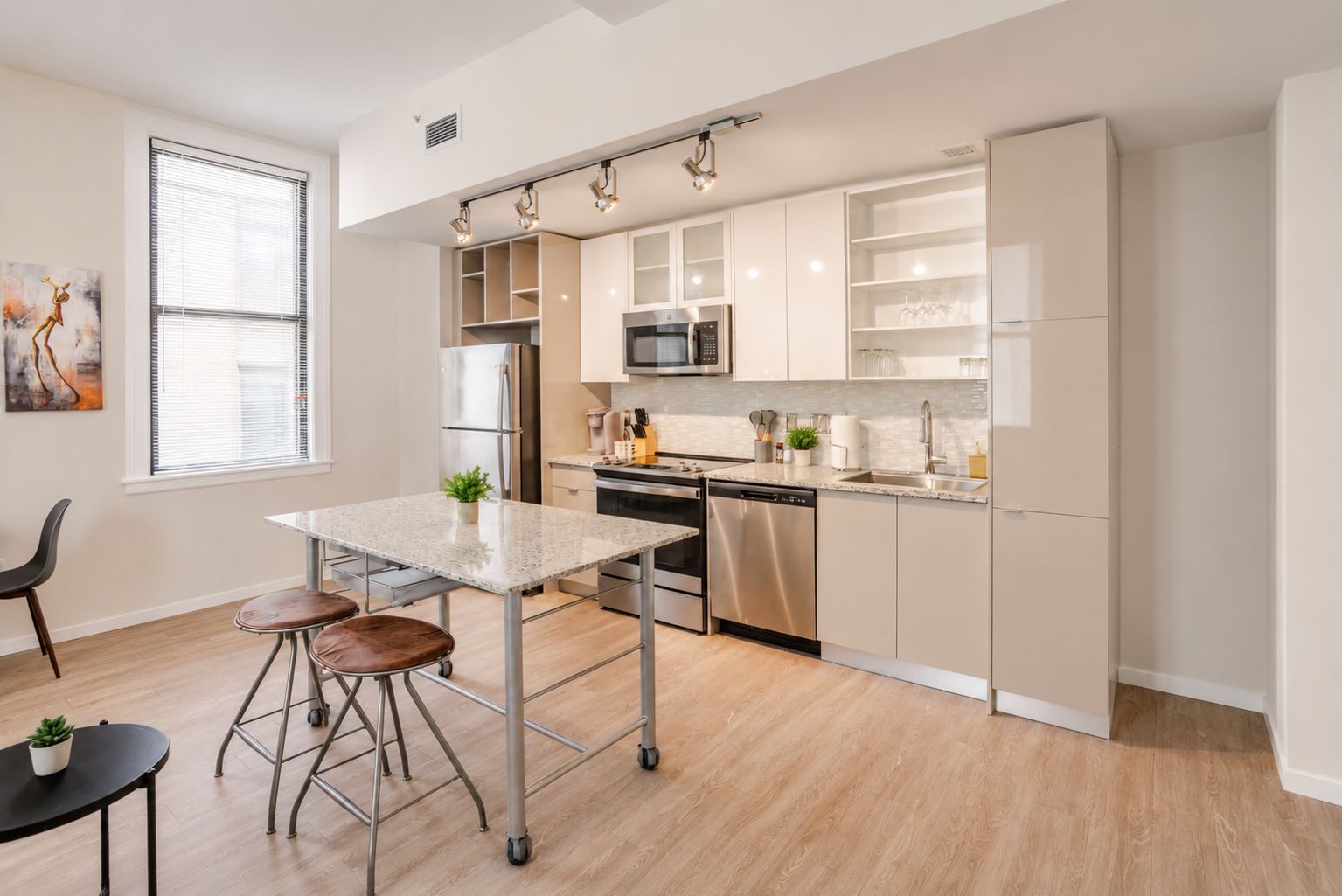 A modern kitchen with a dining area, stainless steel appliances, and a window with blinds.