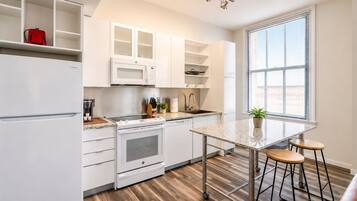 Una cocina moderna con armarios blancos, microondas integrado, estufa y una encimera con taburetes.