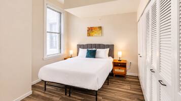 A bedroom with a bed, bedside tables, a window with blinds, and a wall-mounted artwork.