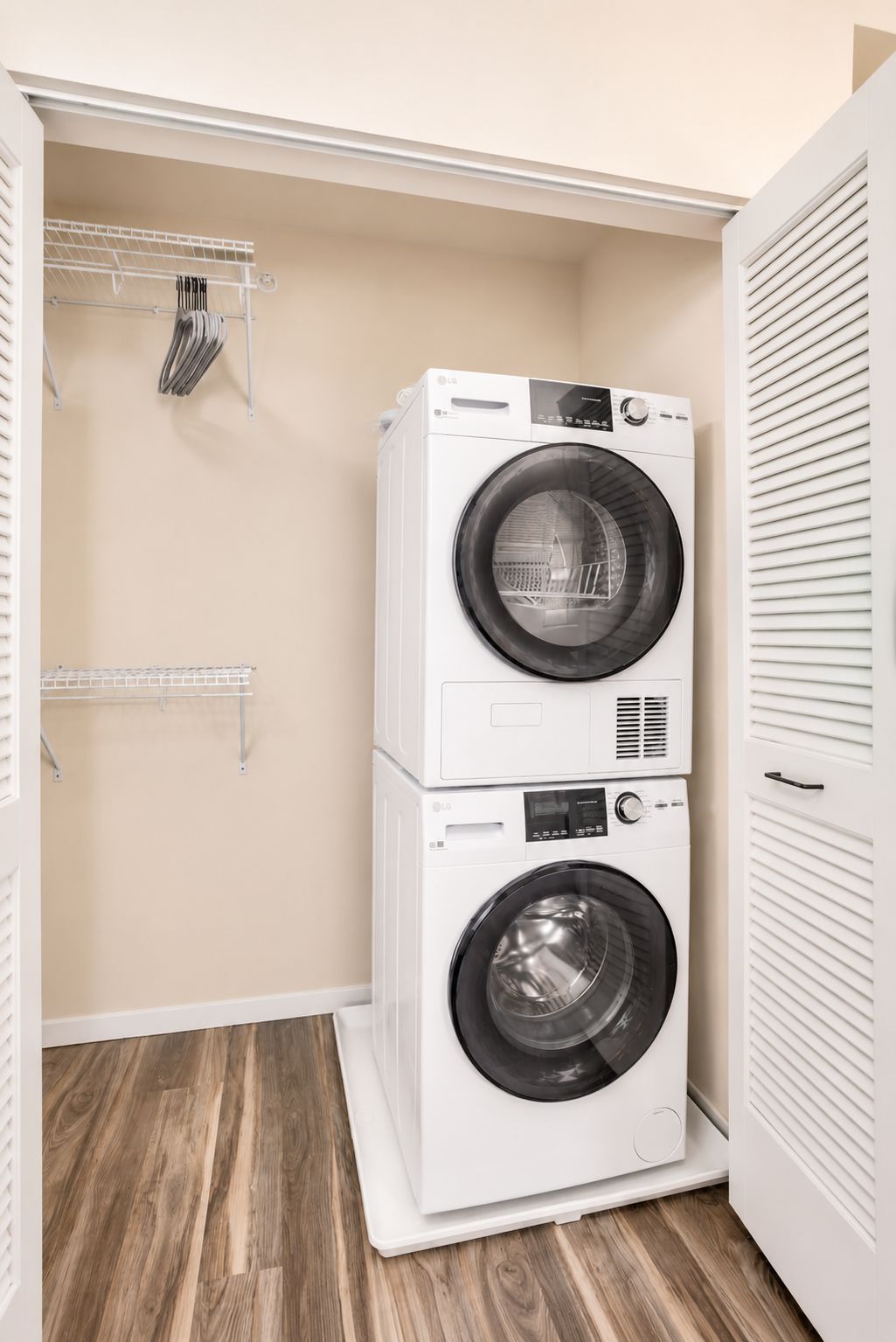 A laundry room with two stacked washing machines, a metal drying rack, and a wooden floor.