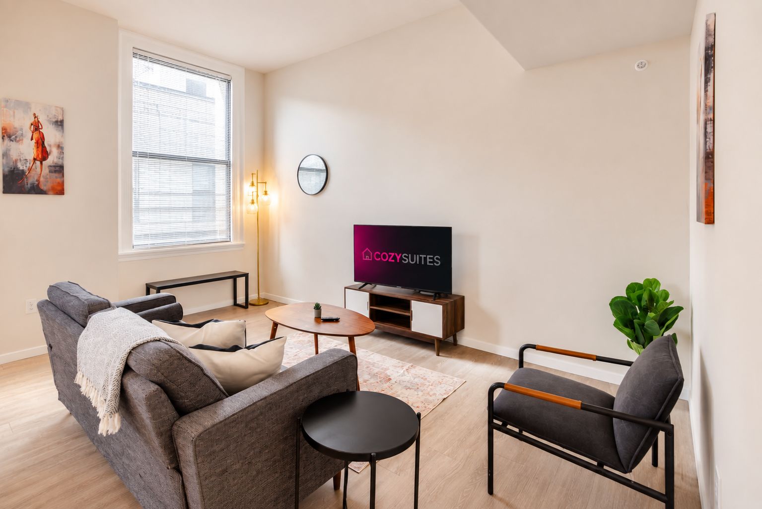 A modern living room with a sofa, coffee table, and TV, featuring a 'COZY SUITES' sign.