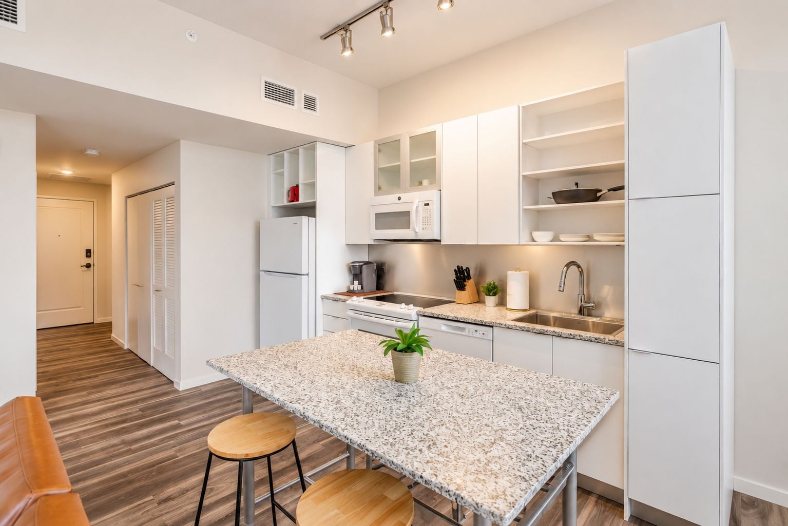 A modern kitchen with white cabinetry, a granite countertop, a built-in microwave, and a stainless steel sink.
