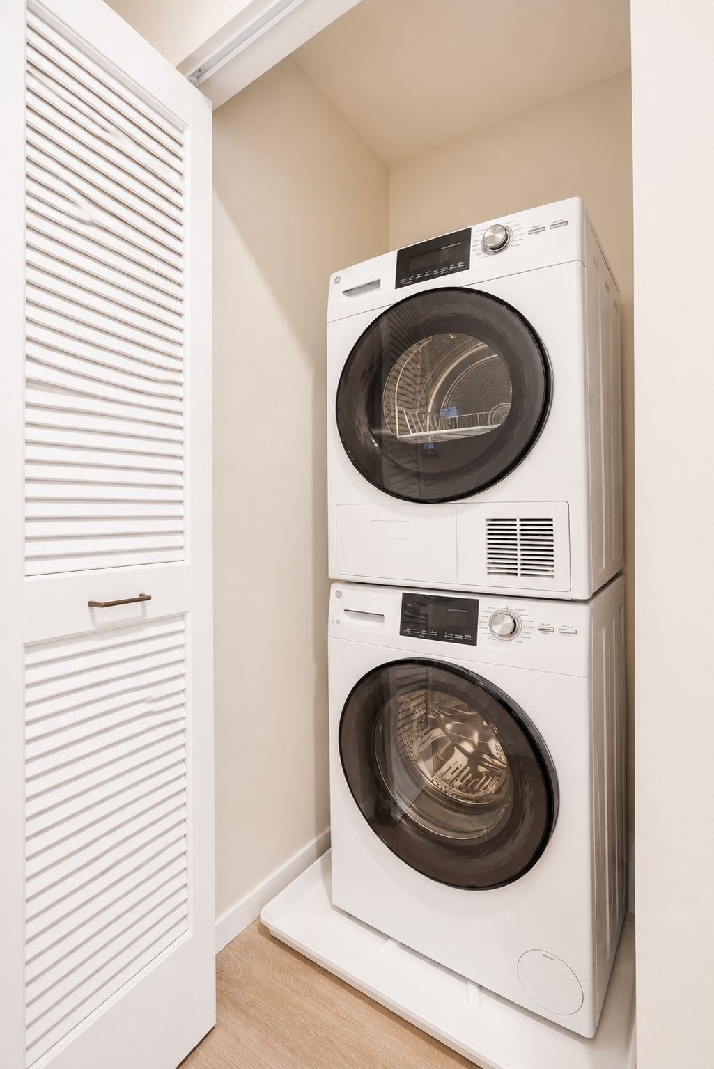 A stacked washer and dryer unit in a laundry room with a white door and a wooden floor.