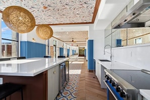 A modern kitchen with a central island, a large window, and a patterned ceiling. - CozySuites - Sky Central (Cincinnati)