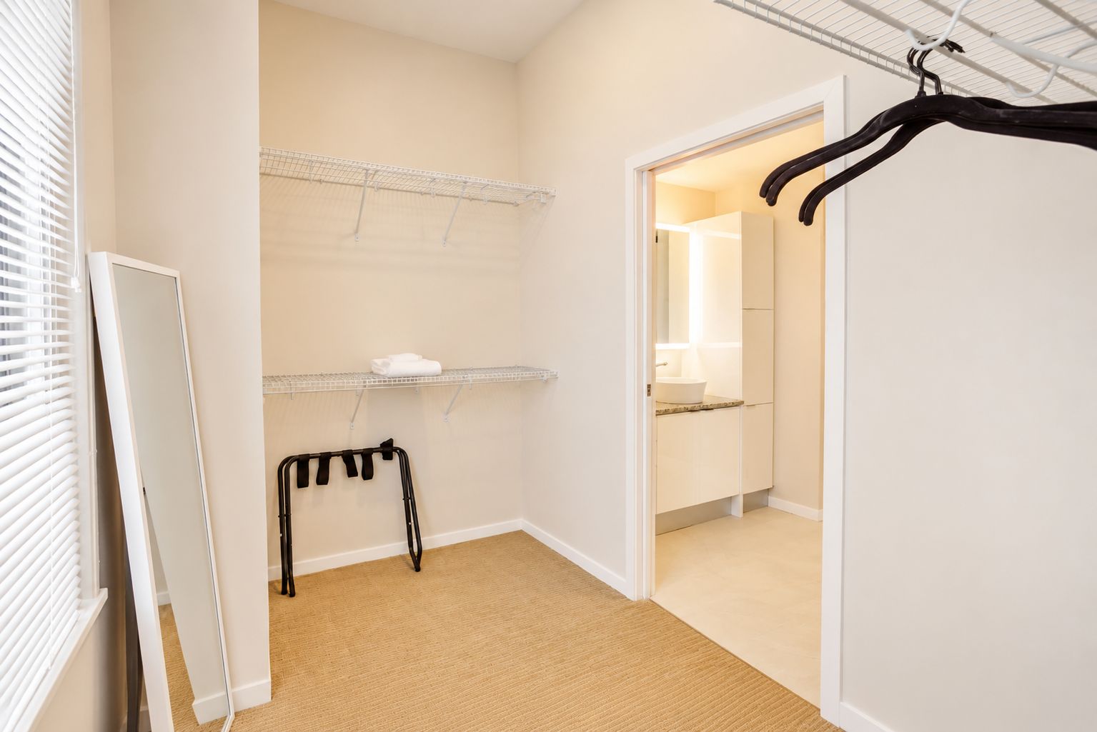 A hallway with a metal rack, a small table with a white object, and a door leading to a bathroom.
