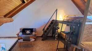 Ett mysigt sovrum på vinden med en våningssäng, en liten soffa, ett skrivbord och en trappa.
