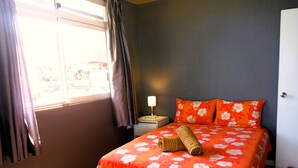 A bedroom with a bed, curtains, a nightstand, a lamp, and a window.