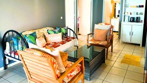 A living room with a sofa, chairs, a coffee table, and a kitchen area with cabinets and appliances.