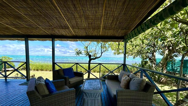 A covered outdoor seating area with wicker furniture and a view of the ocean.