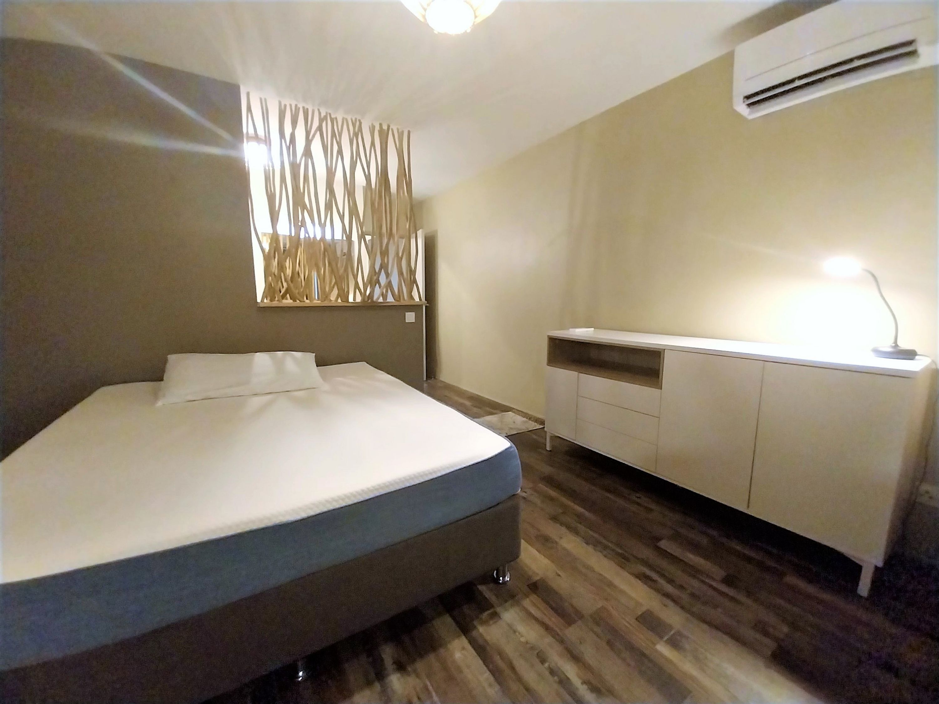 Un dormitorio moderno con una cama, un escritorio y un equipo de aire acondicionado.