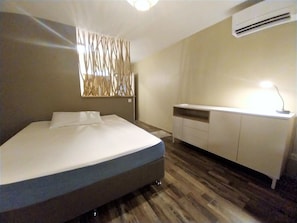 A modern bedroom with a bed, a desk, and an air conditioning unit.