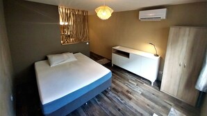 A modern hotel room with a bed, a bedside table, a wardrobe, and a wall-mounted air conditioner. - Tahiti - Urban Maohi Cottage (Papeete)