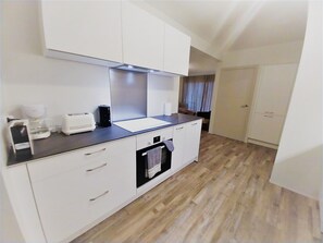 A compact kitchen with white cabinets, a black countertop, a coffee maker, a toaster, and a small oven.