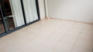 A room with a tiled floor, a sliding glass door with white curtains, and a white wall with a white pipe. - Tahiti - Urban Maohi Cottage (Papeete)