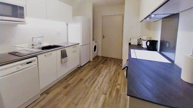 A compact kitchen with white cabinetry, a microwave, a washing machine, and a coffee maker. - Tahiti - Urban Maohi Cottage (Papeete)