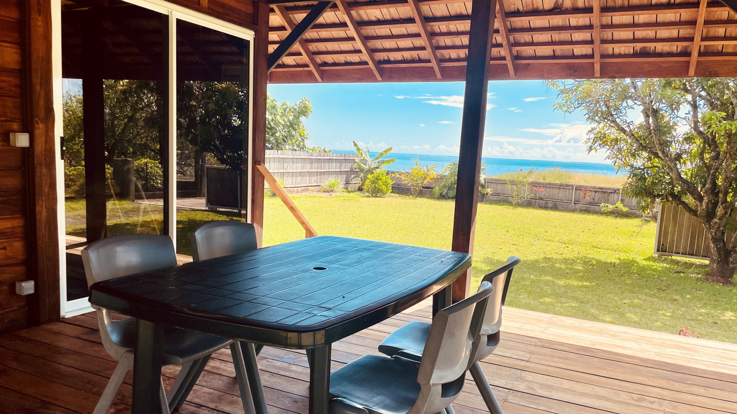 A covered patio with a table and chairs, overlooking a grassy yard and the ocean.