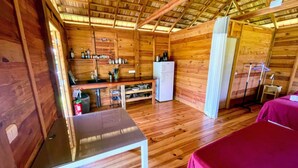 Une petite cabane en bois comprenant un coin cuisine, une petite table et un lit.