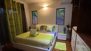 Une chambre à coucher avec un grand lit, une table de chevet, une commode et deux fenêtres équipées de stores.