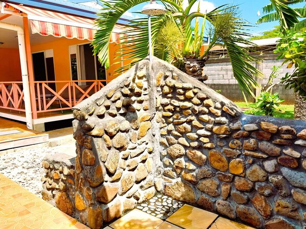 A stone wall with a tiled floor leading to a building with a striped awning. - Tahiti - Lihei Pool House (Faaa)