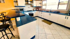 A kitchen with a central island, bar stools, a microwave, stove, and a window with blinds. - Tahiti - Lihei Pool House (Faaa)