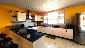 A kitchen with a central island, white cabinets, a stainless steel refrigerator, and a window providing natural light. - Tahiti - Lihei Pool House (Faaa)