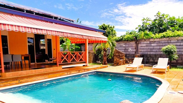 A swimming pool with a tiled deck, lounge chairs, and a covered patio area with outdoor furniture. - Tahiti - Lihei Pool House (Faaa)