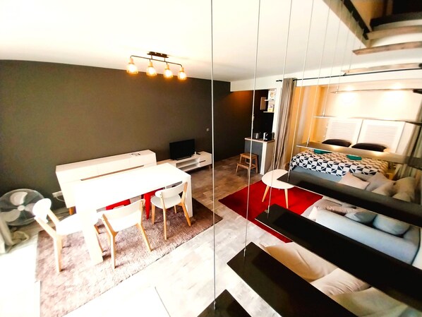 A modern, compact living space with a dining area, a bed with a geometric-patterned duvet, and a television.