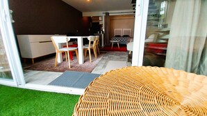 A modern interior with a dining area, a sofa, and a glass door leading to a balcony with artificial grass. - Tahiti - Urban Escape (Papeete)