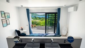 Un baño moderno con lavamanos dobles, un ventanal con vistas a la vegetación y un cuerpo de agua, y una mesita redonda con una silla.
