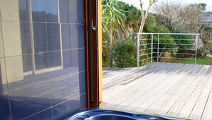 Un bain à remous sur une terrasse en bois, avec vue sur un bâtiment et la végétation environnante.