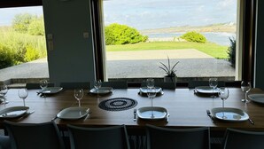Un coin repas avec une table dressée pour six personnes, offrant une vue panoramique sur un lac et la verdure environnante.