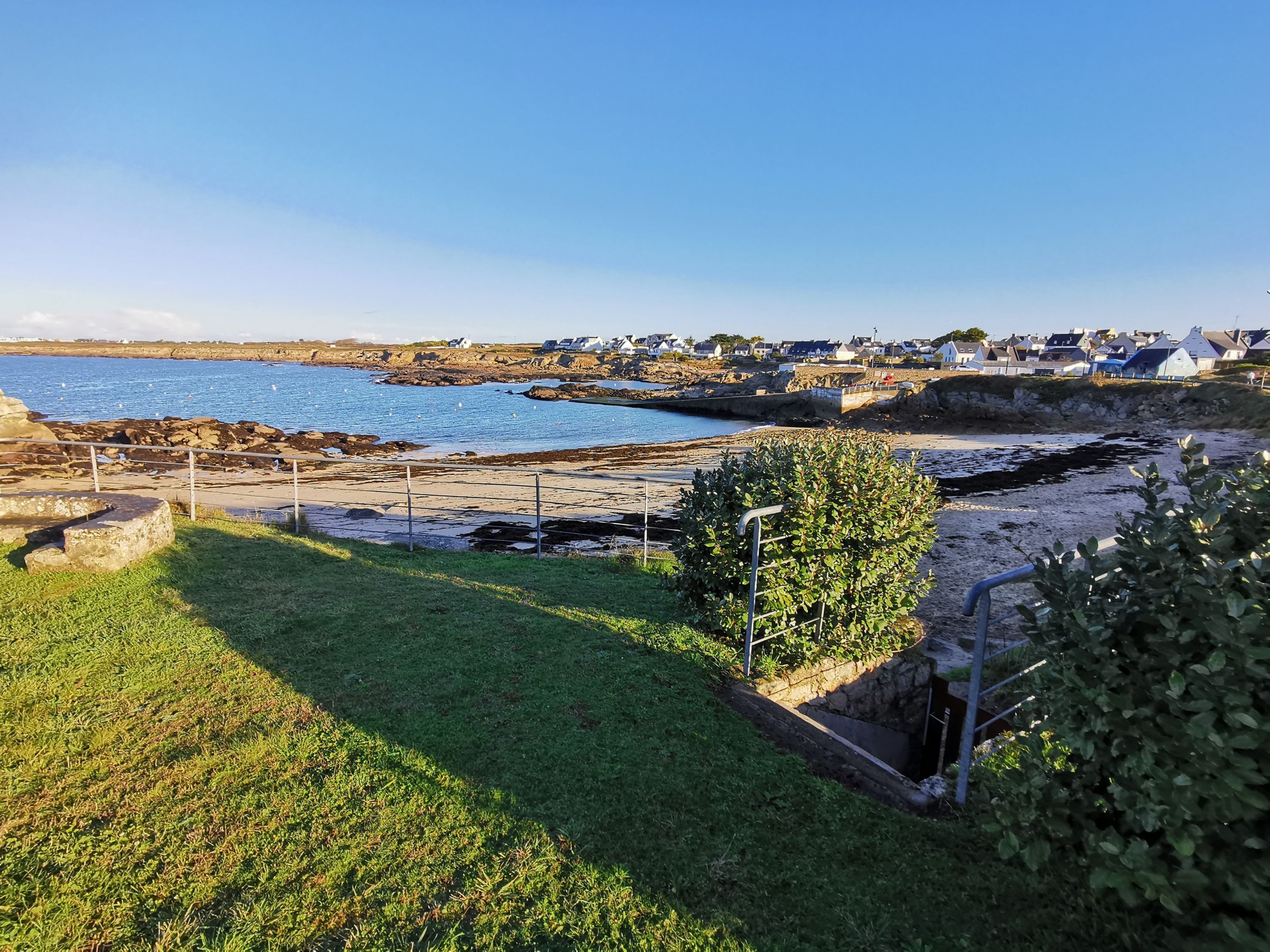 A coastal landscape with a grassy foreground, rocky shoreline, and a distant village.