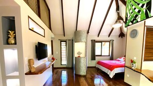 Une chambre d’hôtel avec un plancher en bois, un lit recouvert d’une courtepointe rouge et blanche, un téléviseur fixé au mur et une fenêtre avec des rideaux.