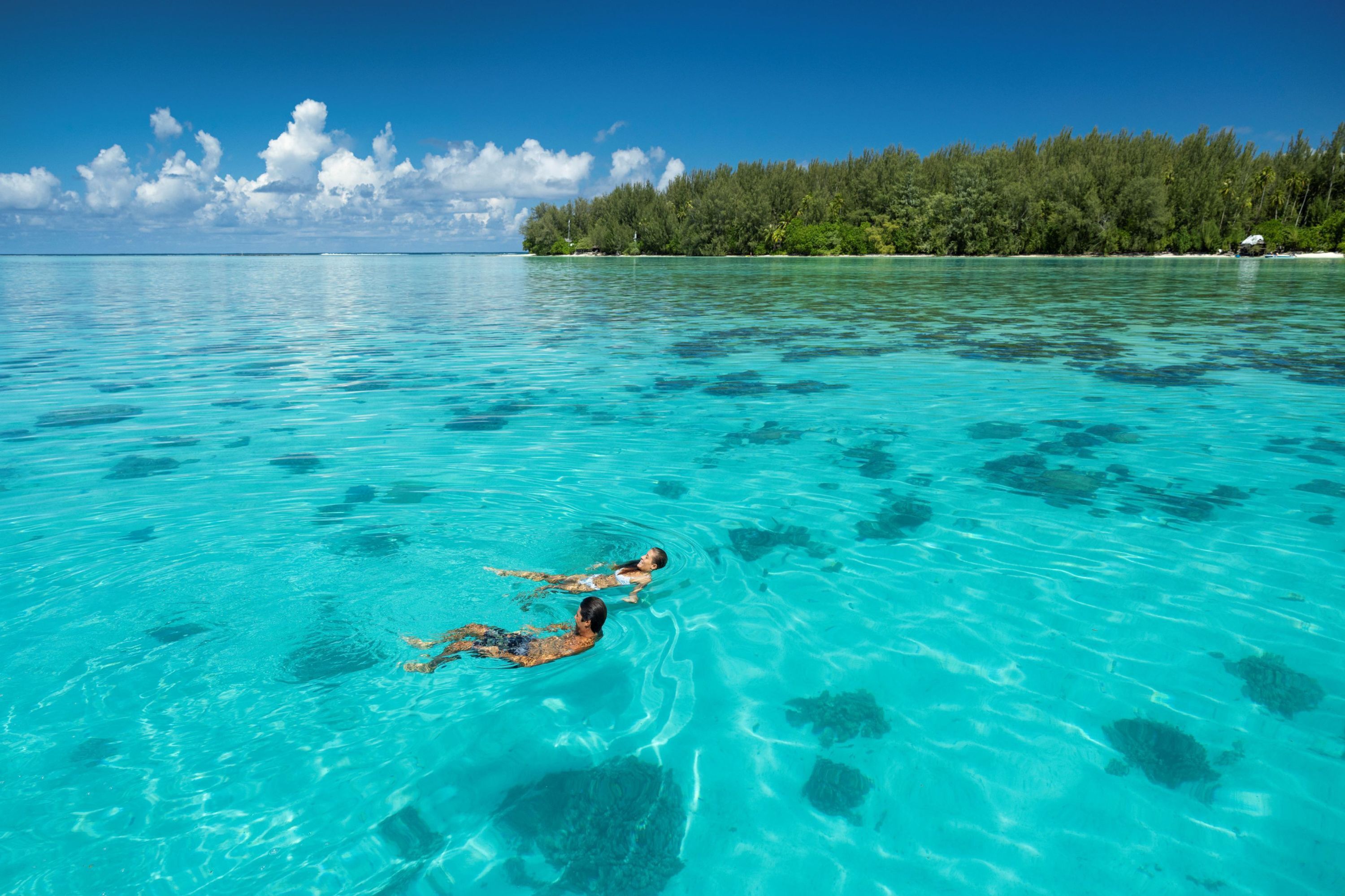 A clear turquoise sea with two people swimming.