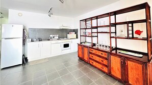 A modern kitchen with white cabinets, a built-in oven, a microwave, and a wooden cabinet with glass shelves. - Tahiti - Toke Condo in Faa a (Faaa)