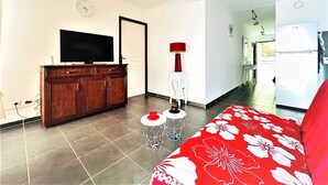 A bedroom with a bed, a TV, a wooden cabinet, a red lamp, and a white side table. - Tahiti - Toke Condo in Faa a (Faaa)