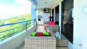 A balcony with wicker furniture, a potted plant, and a view of greenery. - Tahiti - Toke Condo in Faa a (Faaa)
