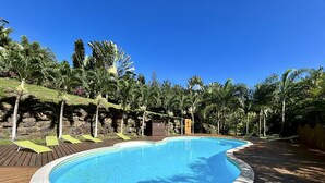 A swimming pool with a wooden deck, surrounded by palm trees and a rocky hillside. - Moorea - Villa Ana Mua (Moorea-Maiao)