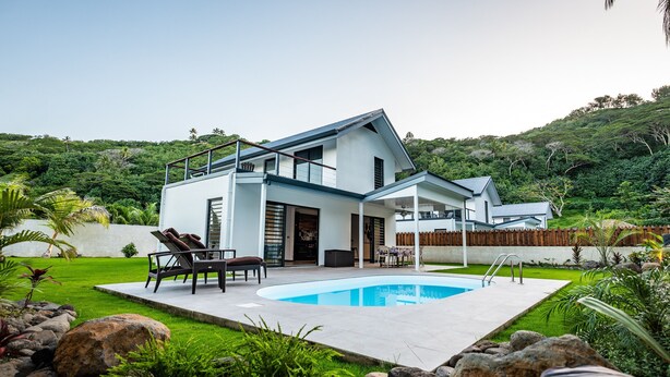 Une maison moderne dotée d’une piscine, d’un patio avec mobilier d’extérieur et d’un jardin luxuriant.