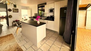A modern kitchen with a central island, white cabinetry, a microwave, and a refrigerator. - Tahiti - The Cozy Corner (Paea)