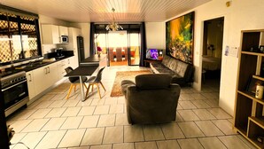 A modern kitchen with a dining area, a living room with a sofa, and a large painting on the wall. - Tahiti - The Cozy Corner (Paea)
