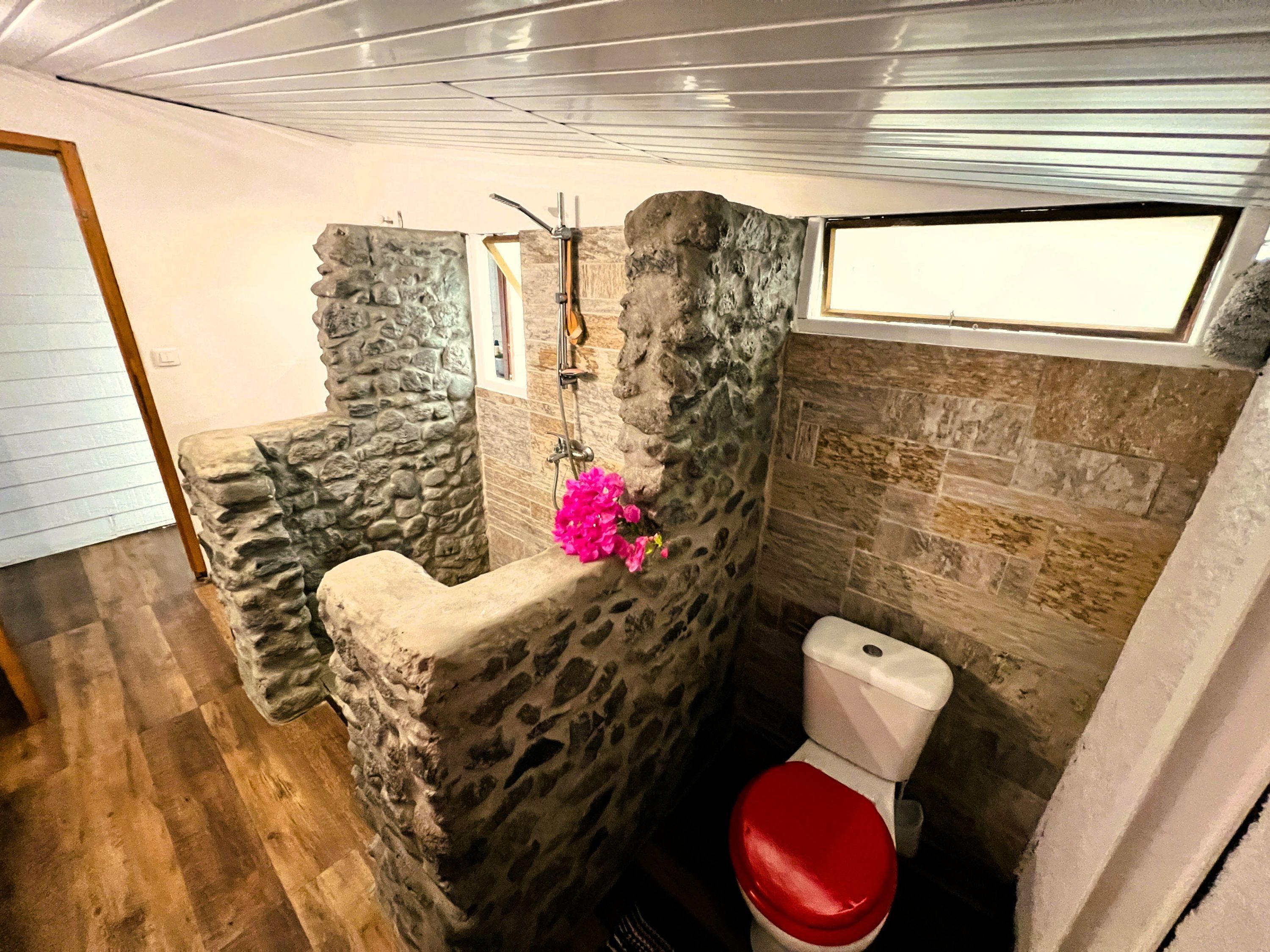 A bathroom with stone walls, a red toilet, and a shower area.