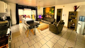 A modern living room with a sofa, a dining table, and a kitchen area. - Tahiti - The Cozy Corner (Paea)