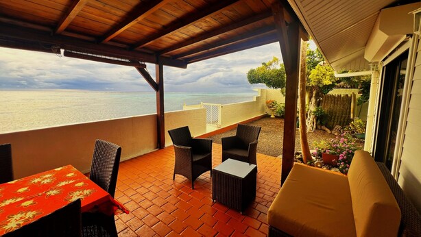 A covered patio with wicker furniture, a table with a floral tablecloth, and a view of the sea. - Tahiti - The Cozy Corner (Paea)