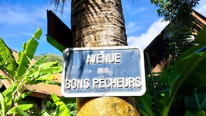 A street sign reading "Avenue des Bons Pêcheurs" mounted on a post with a palm tree and banana plants in the background. - Moorea - Tropical Nest (Moorea-Maiao)