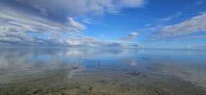 A beach with clear water and a wide view of the sky.